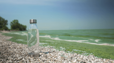 A clear reusable water sits on a pebble beach