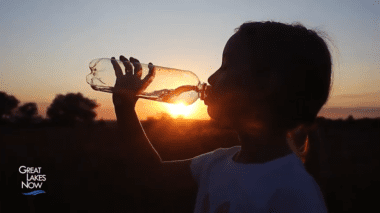 A child drinking from a single use bottle. A blurred sunset is in the background.